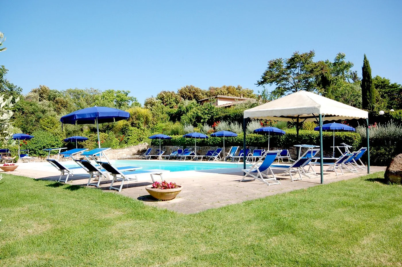 Piscina con lettini blu, ombrelloni e gazebo circondata da giardino curato