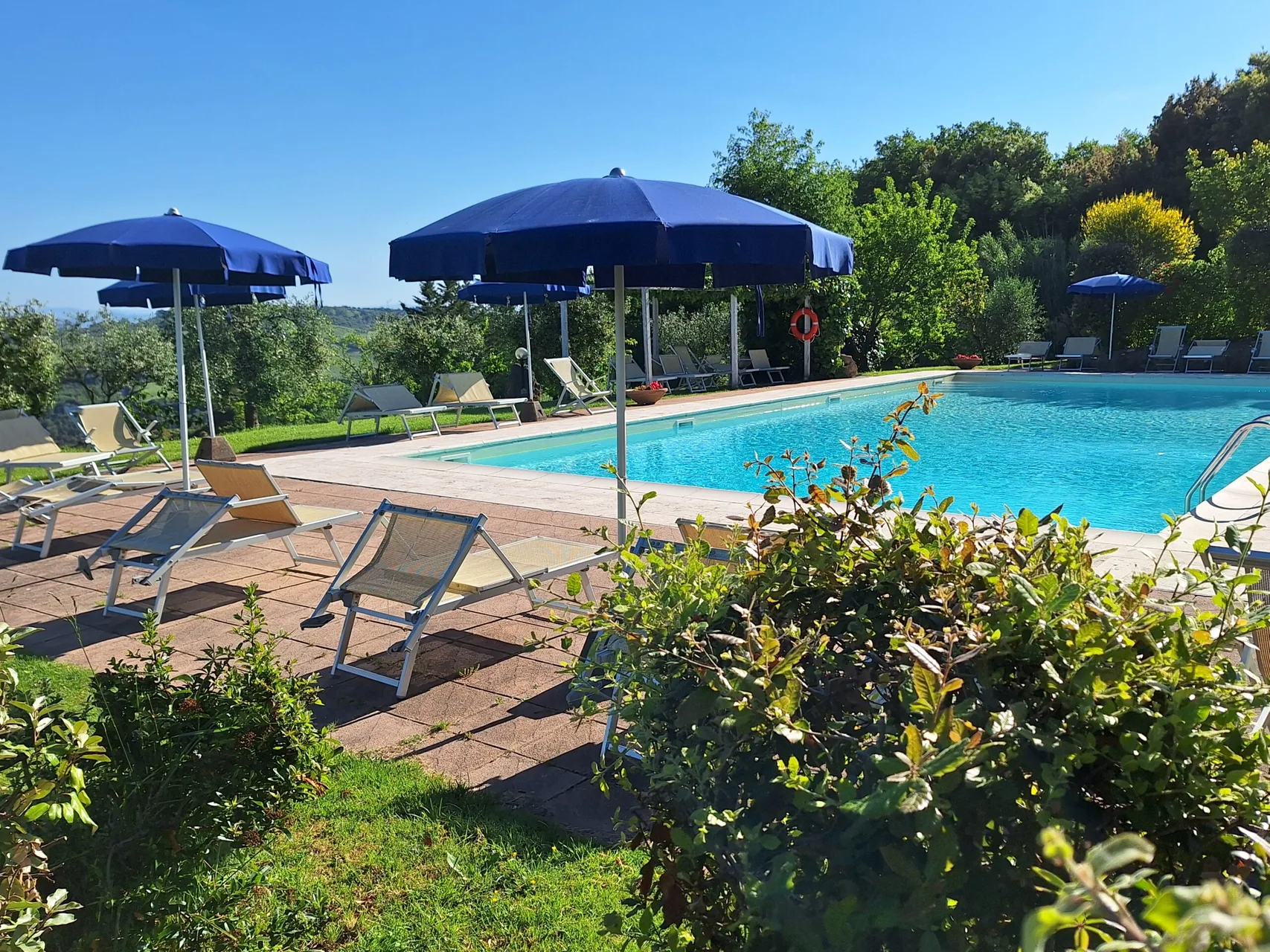 Piscina azzurra con ombrelloni blu e lettini affacciata sul paesaggio collinare