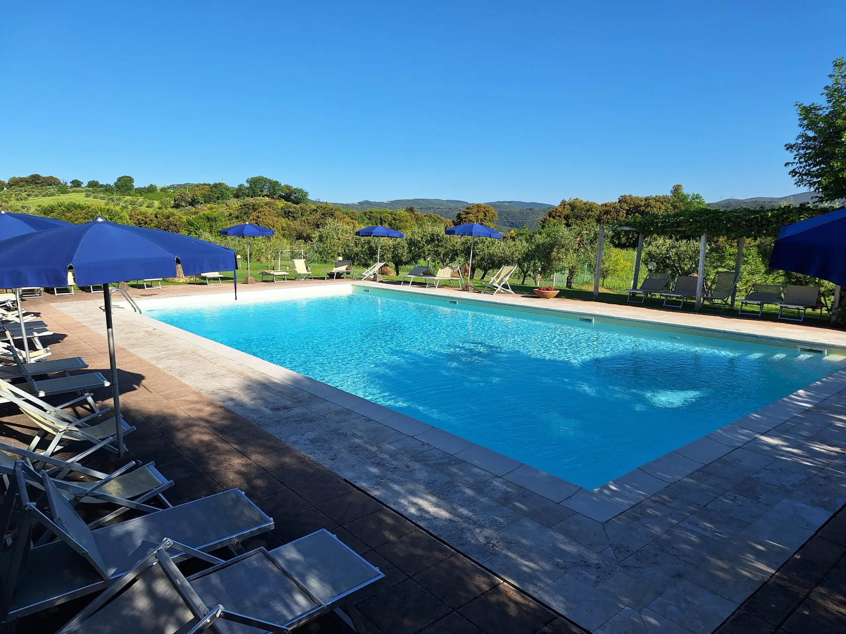 Piscina rettangolare con lettini e ombrelloni blu con vista panoramica sulle colline