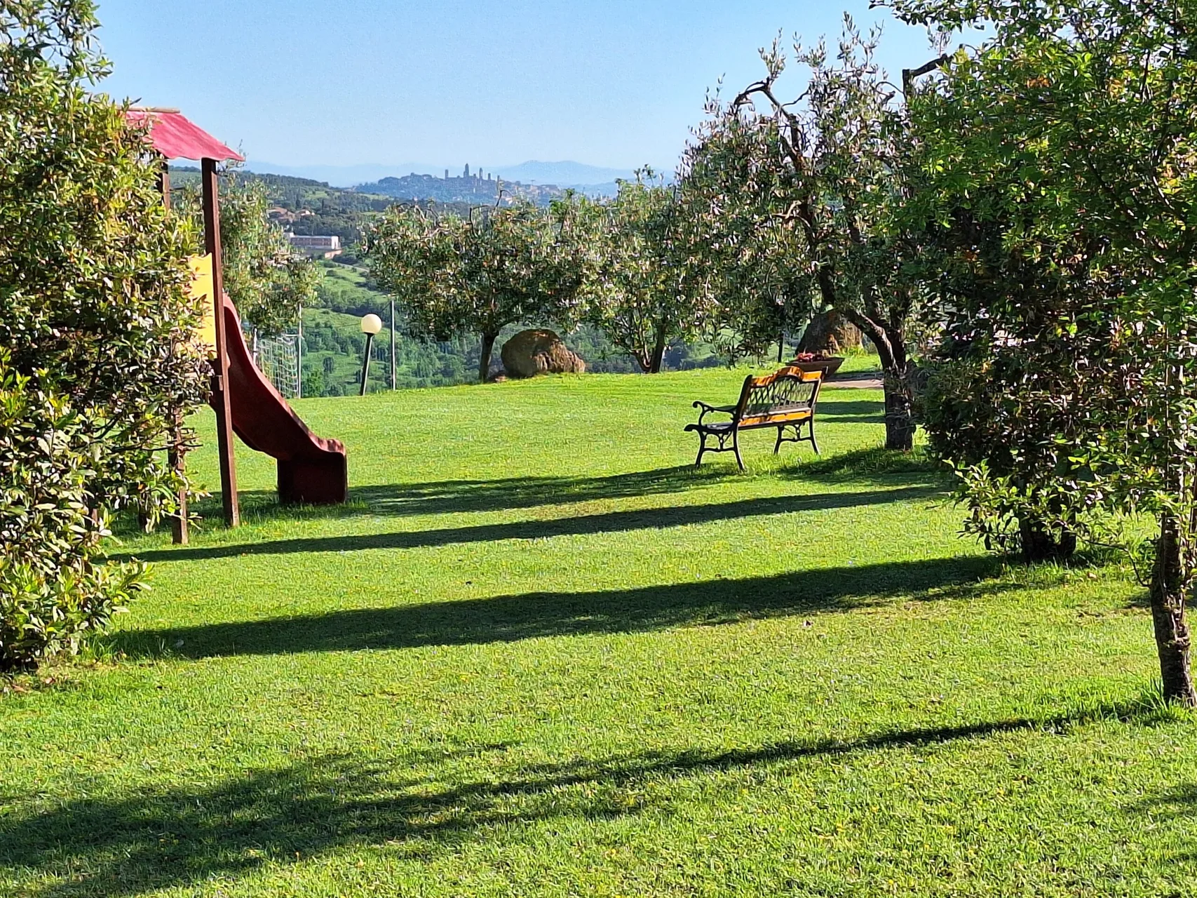 Giardino verde con scivolo per bambini, panchina e vista su San Gimignano in lontananza