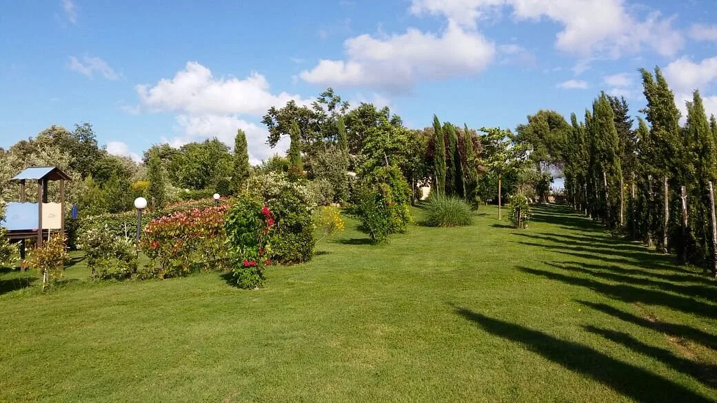 Ampio prato verde con siepi fiorite e viale di cipressi