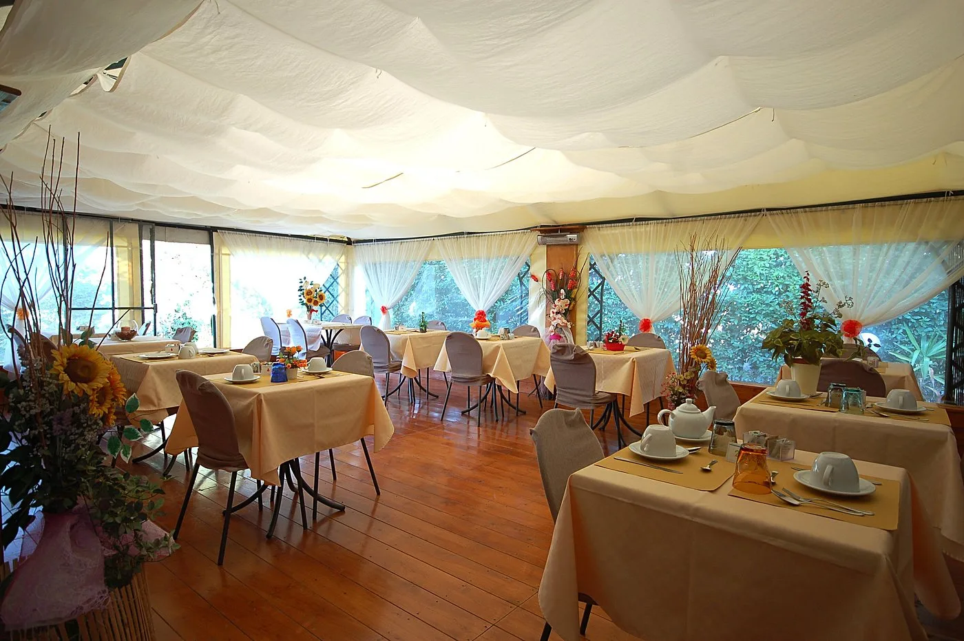 Sala colazione con tavoli apparecchiati, tende bianche e decorazioni floreali