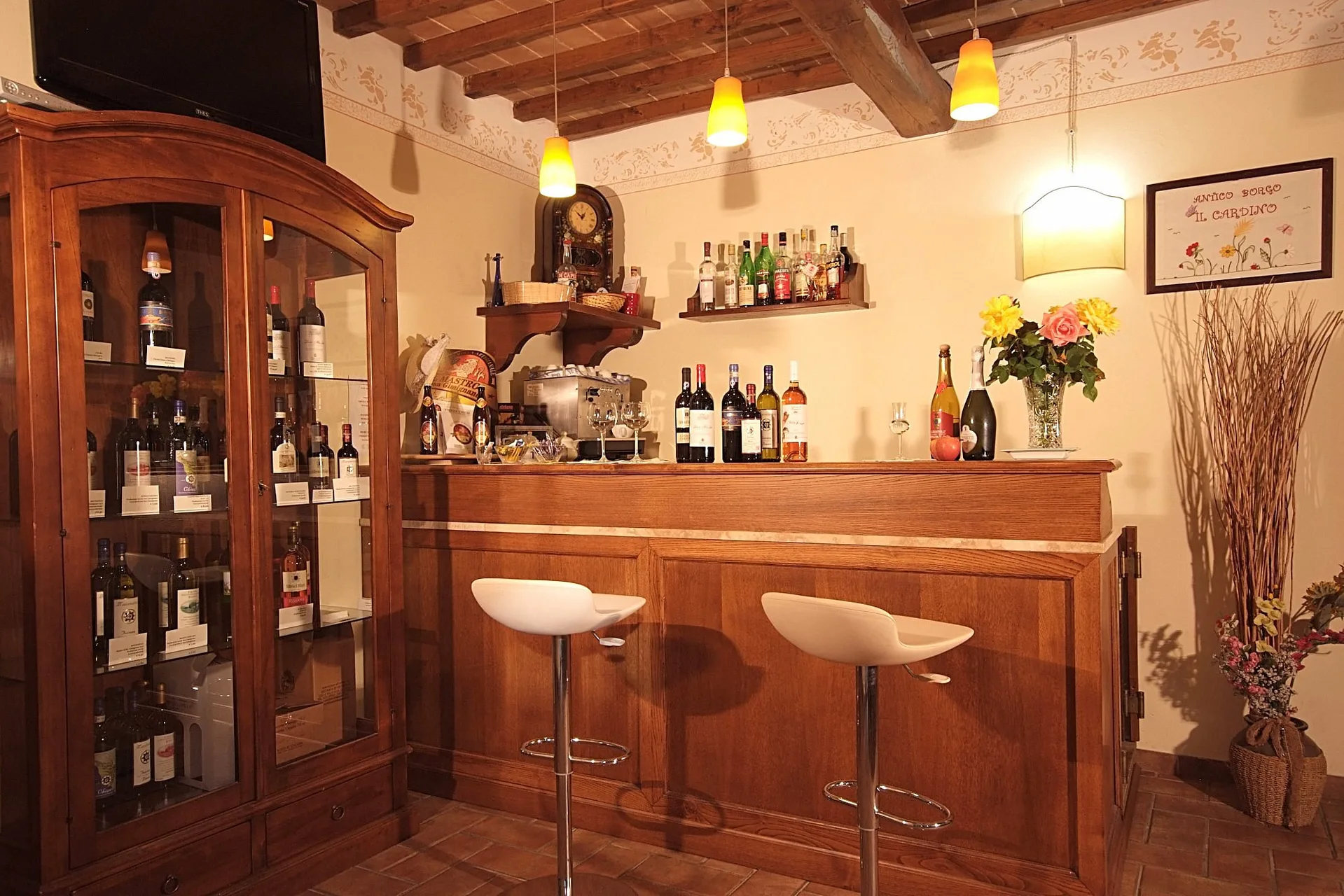 Angolo bar in legno con bottiglie di vino, sgabelli e travi a vista