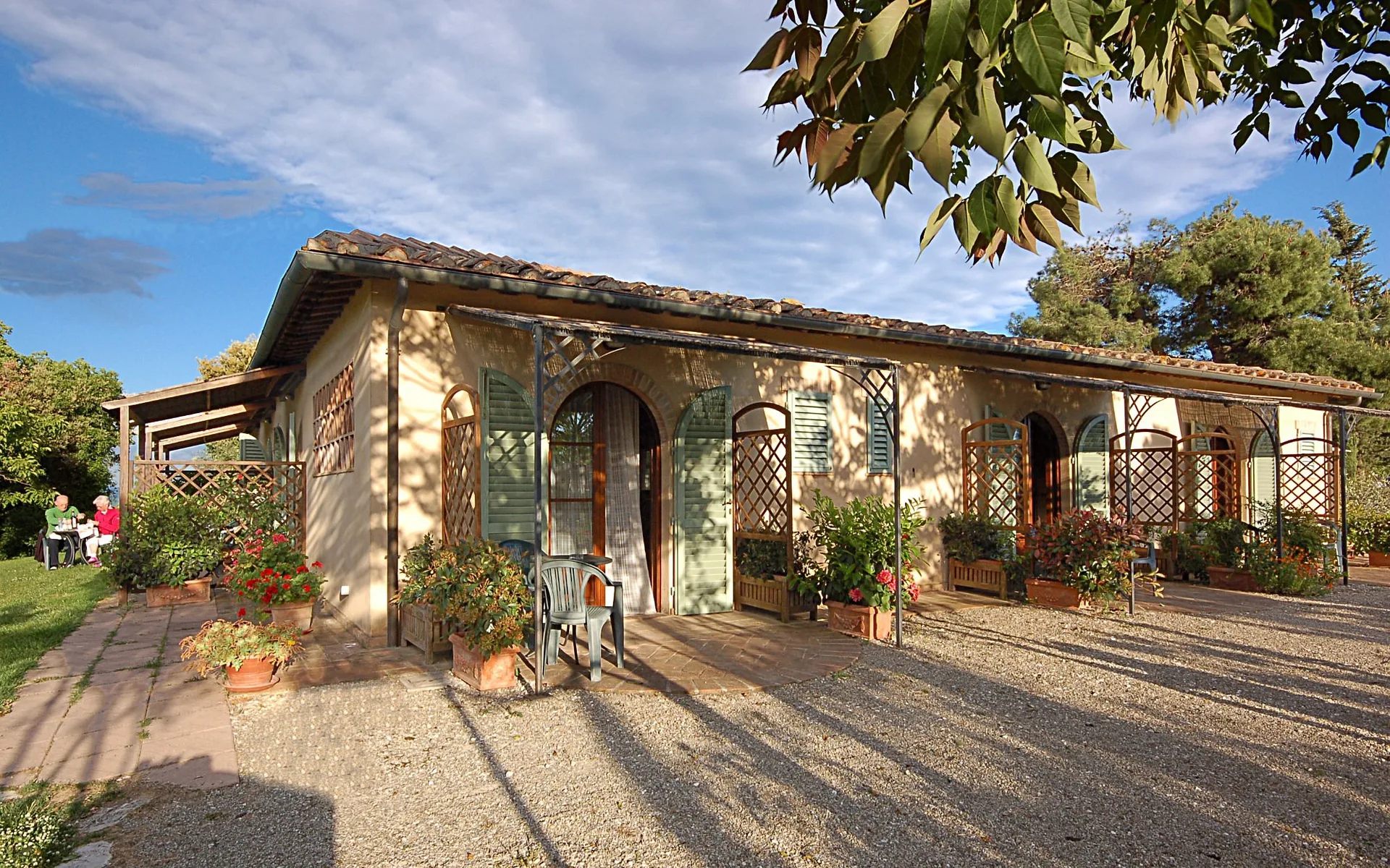 Casale toscano con portico, persiane verdi e piante in vaso fiorite