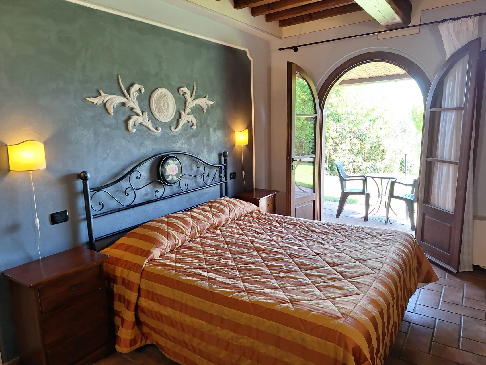 Camera con parete grigia decorata, letto matrimoniale e porta ad arco affacciata sul giardino
