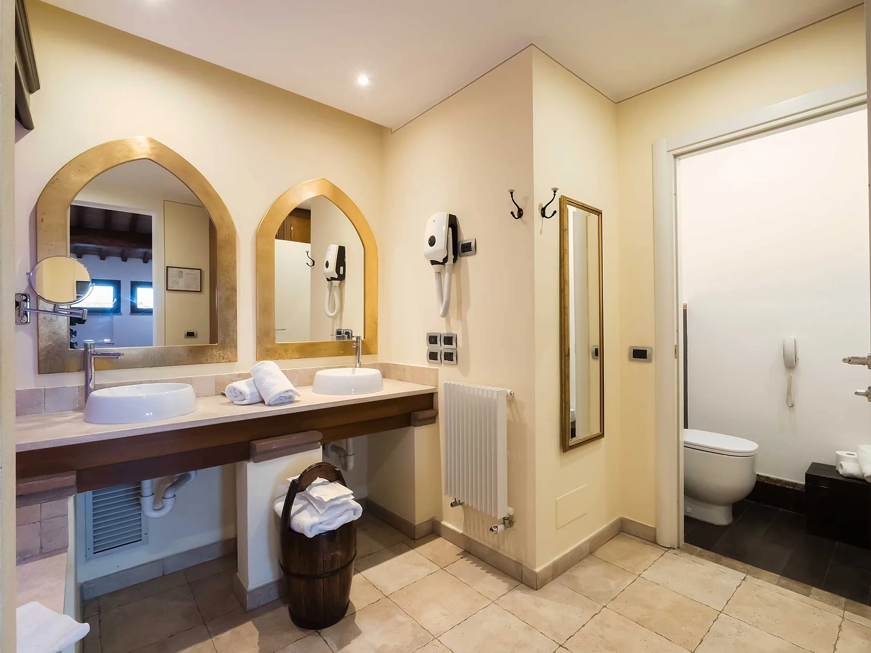 Bagno con doppio lavabo, specchi ad arco dorati, radiatore e area toilette separata