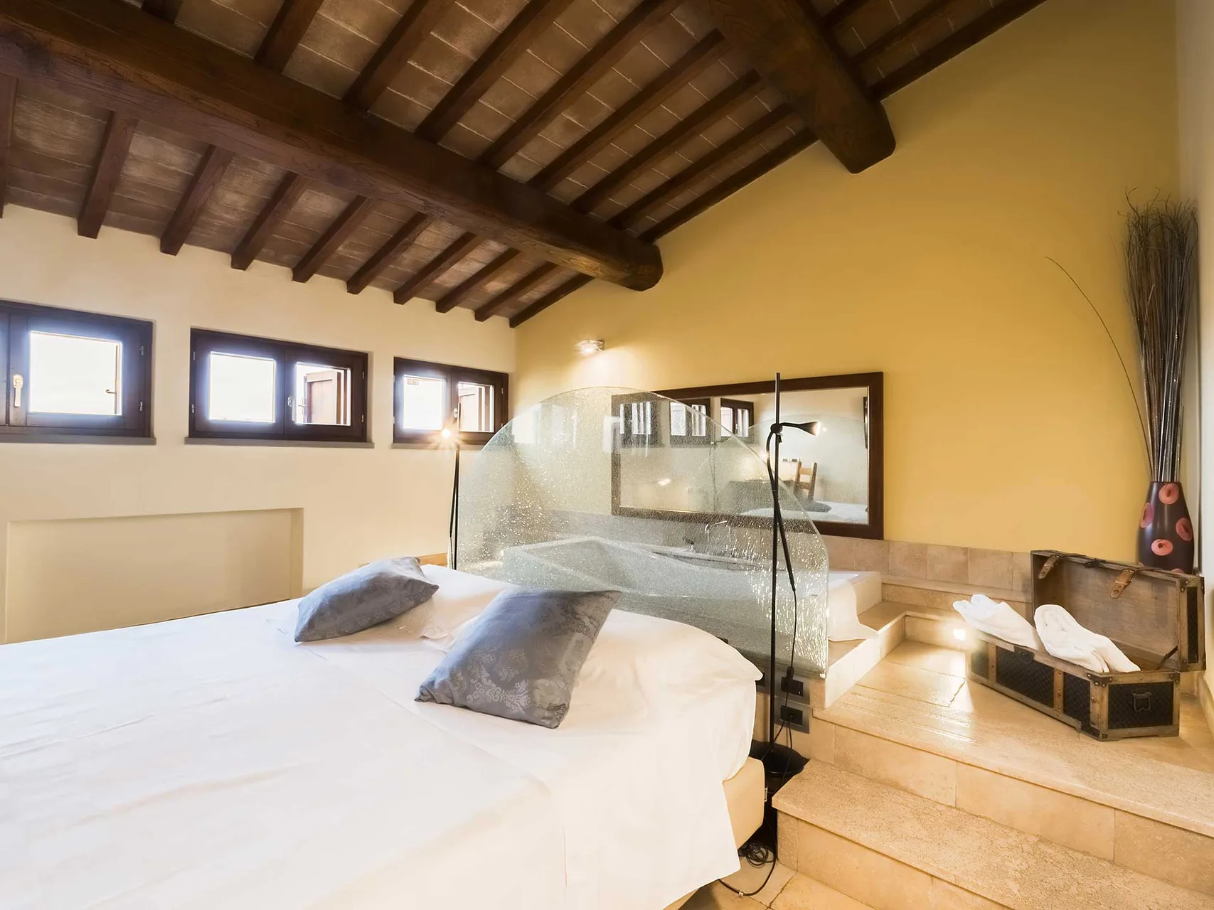 Suite con soffitto in travi di legno, letto rotondo e vasca rialzata con parete in vetro