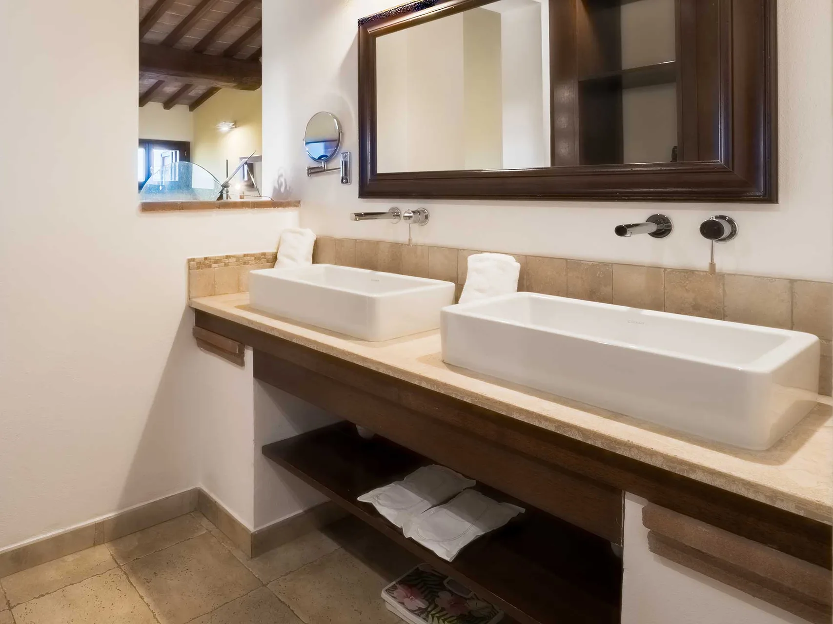 Bagno con doppio lavabo bianco su piano in marmo, specchio con cornice in legno e travi a vista