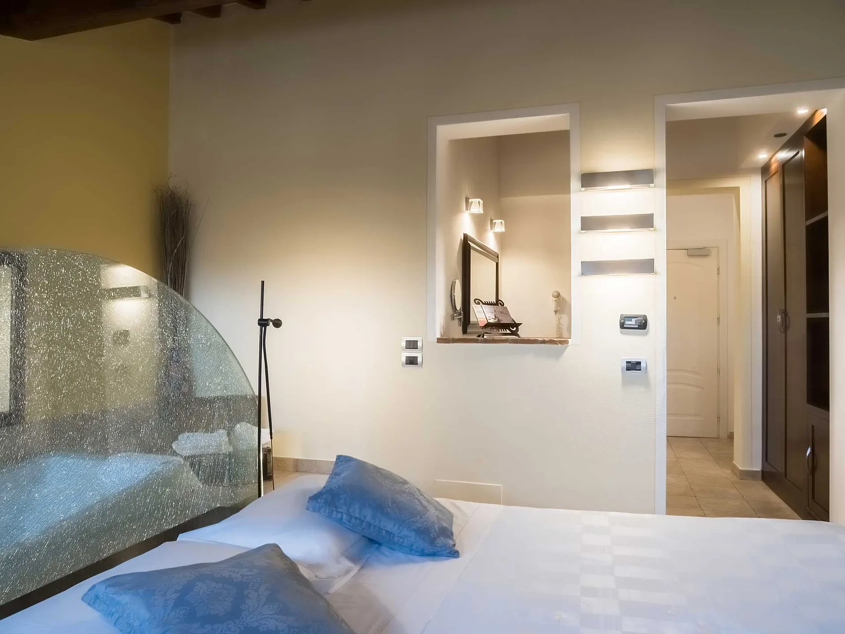 Camera con letto matrimoniale, parete divisoria in vetro verso la vasca e nicchie illuminate