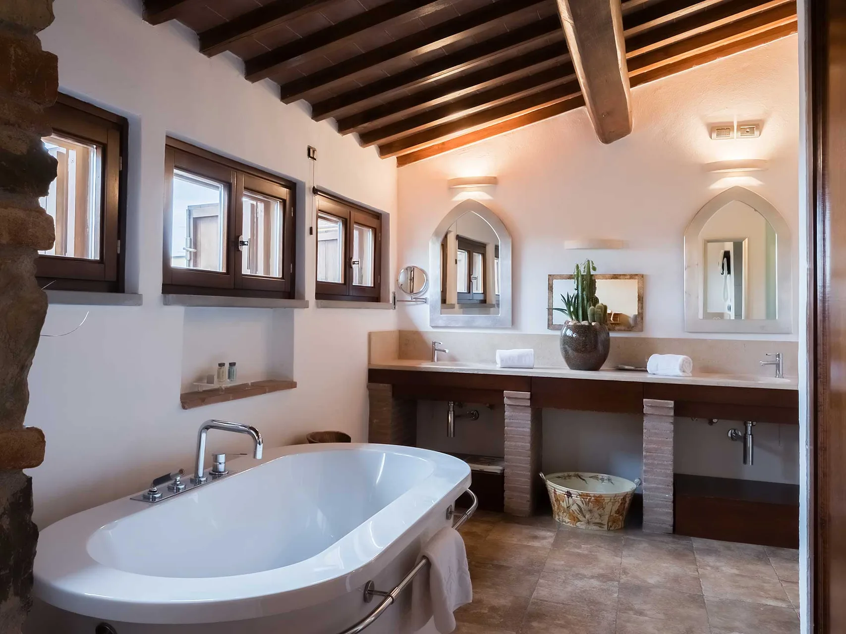Ampio bagno con vasca freestanding, doppio lavabo in marmo, finestre in legno e travi a vista