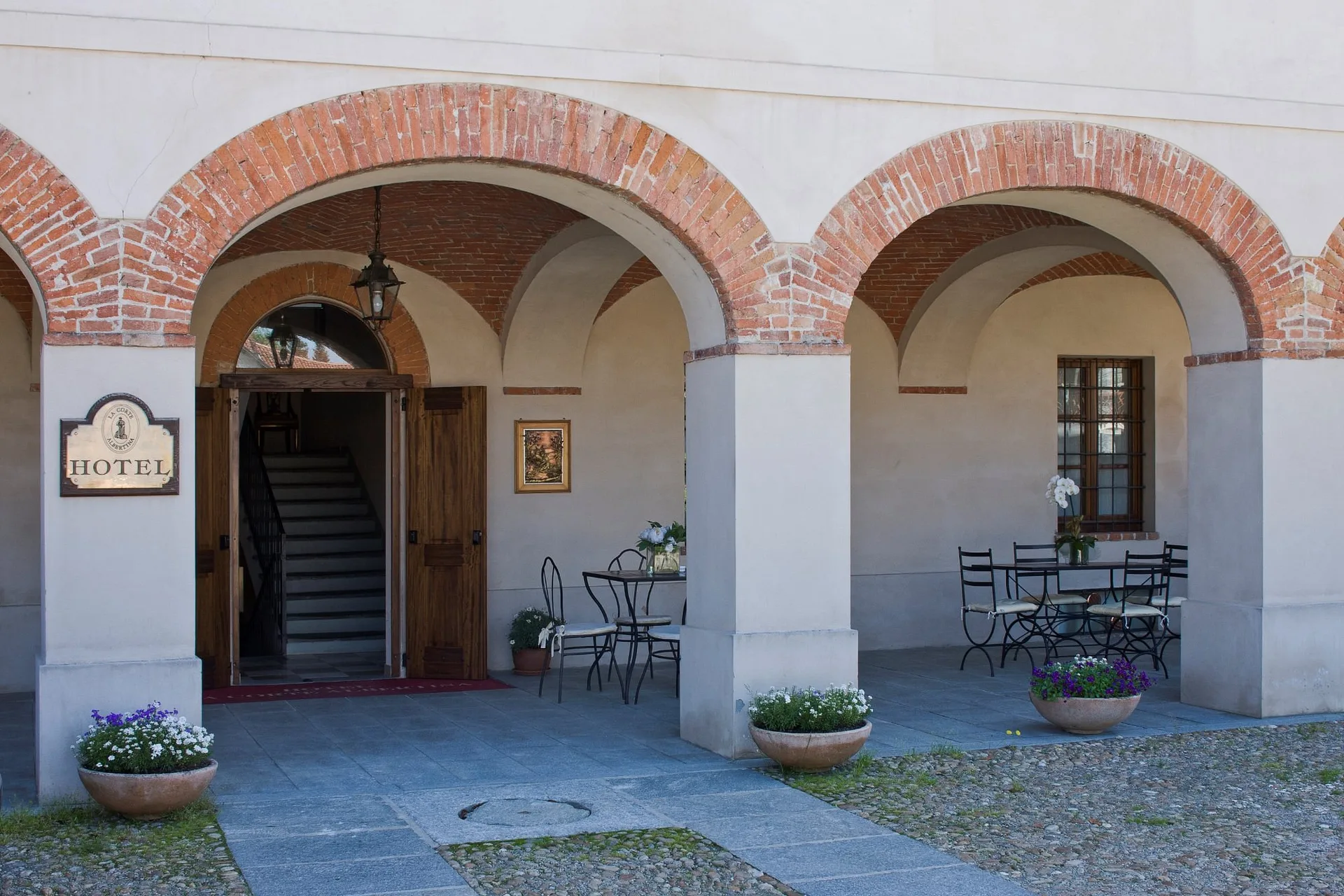 Ingresso dell'hotel con portico ad archi in mattoni, insegna Hotel e tavolini in ferro battuto