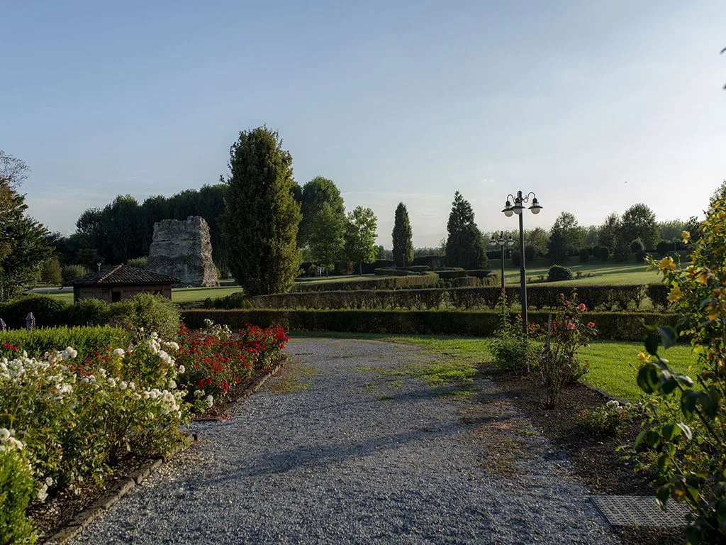 Giardino con vialetto in ghiaia, siepi curate, cespugli fioriti e alberi al tramonto