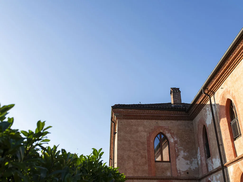 Dettaglio dell'angolo di un edificio storico in muratura rosata con finestre ad arco e cielo azzurro