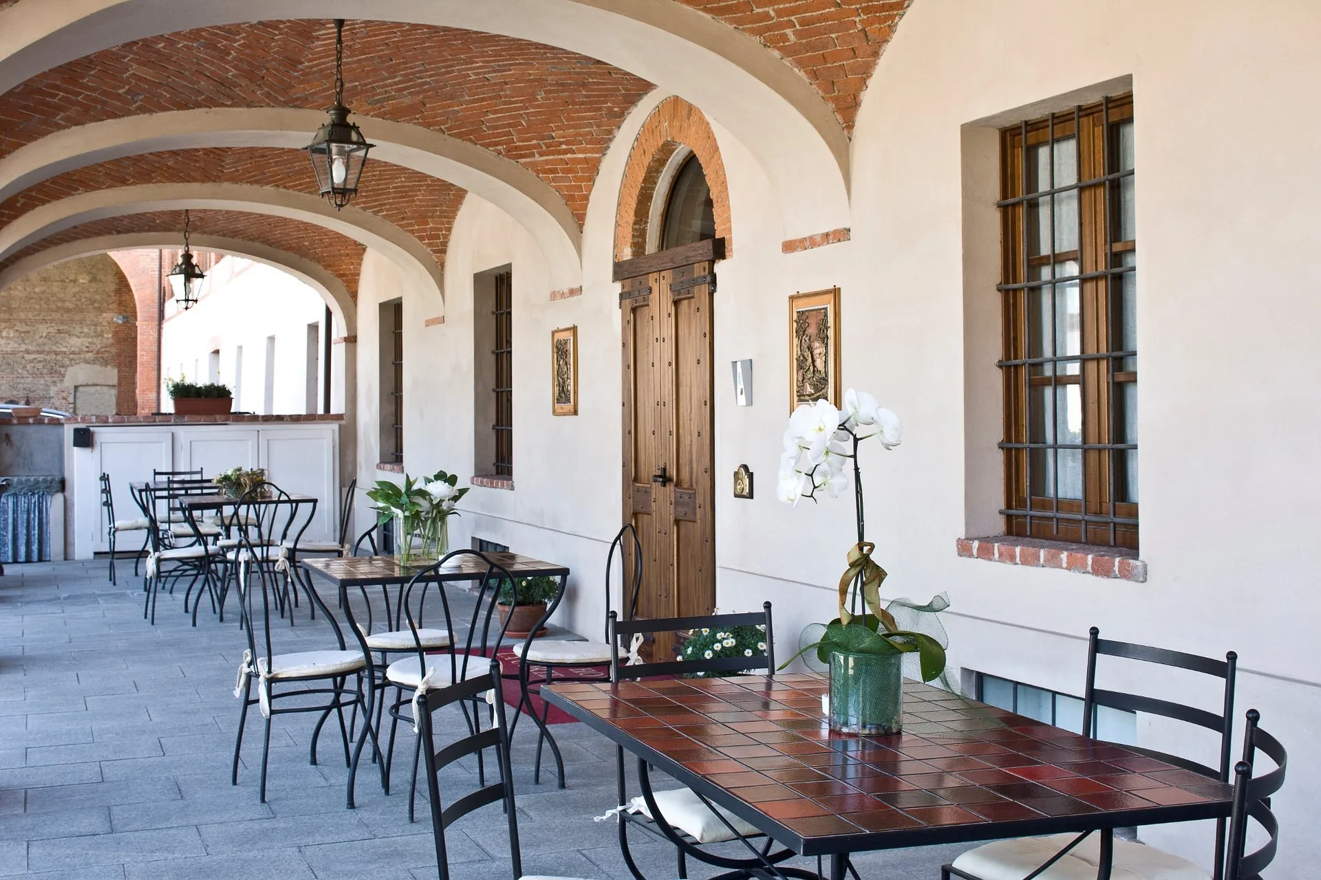 Portico con soffitto a volte in mattoni, tavolini in ferro battuto e orchidee bianche