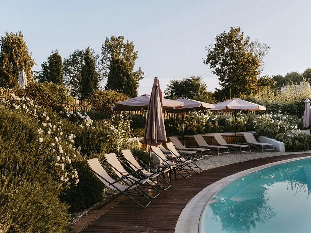Bordo piscina con lettini, ombrelloni e cespugli fioriti circondato dalla vegetazione al tramonto