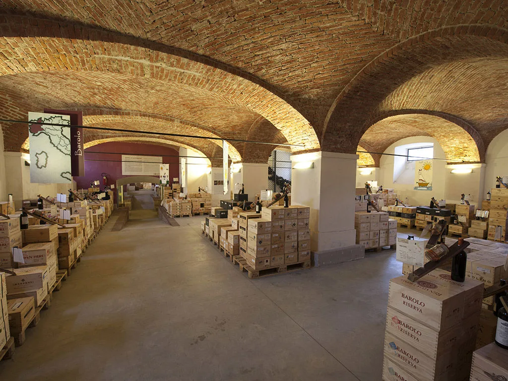 Cantina storica con soffitto a volte in mattoni e casse di vino Barolo impilate