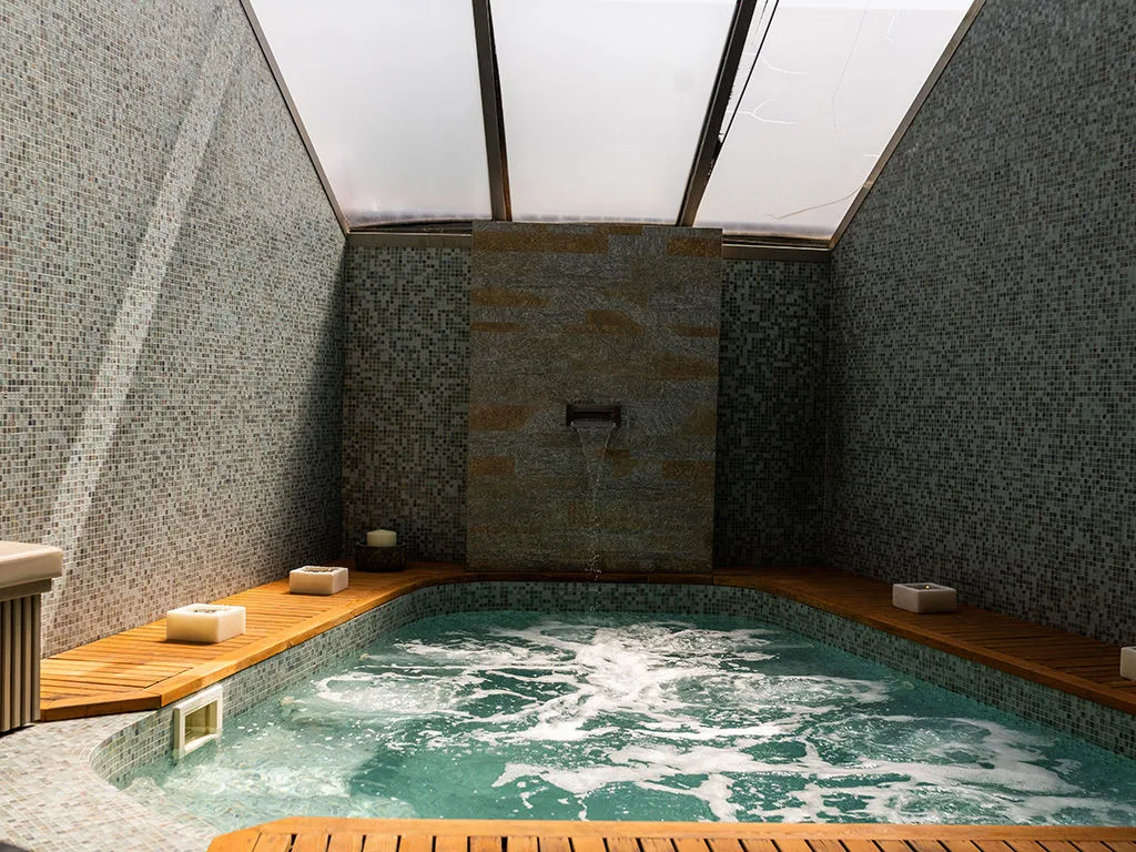 Vasca idromassaggio della spa con mosaico grigio, cascata d'acqua e copertura in vetro