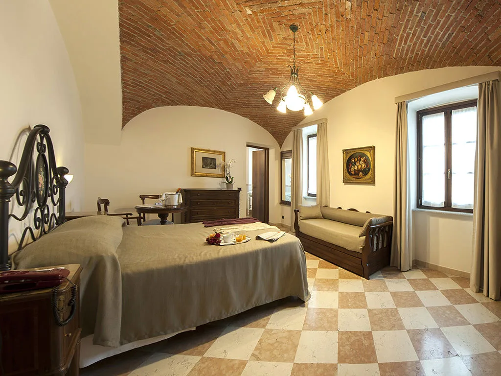 Camera con soffitto a volte in mattoni a vista, letto matrimoniale, pavimento a scacchi e divanetto