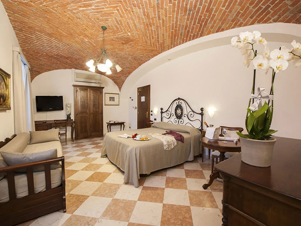 Ampia camera con soffitto a volte in mattoni, letto matrimoniale, divano e orchidee bianche