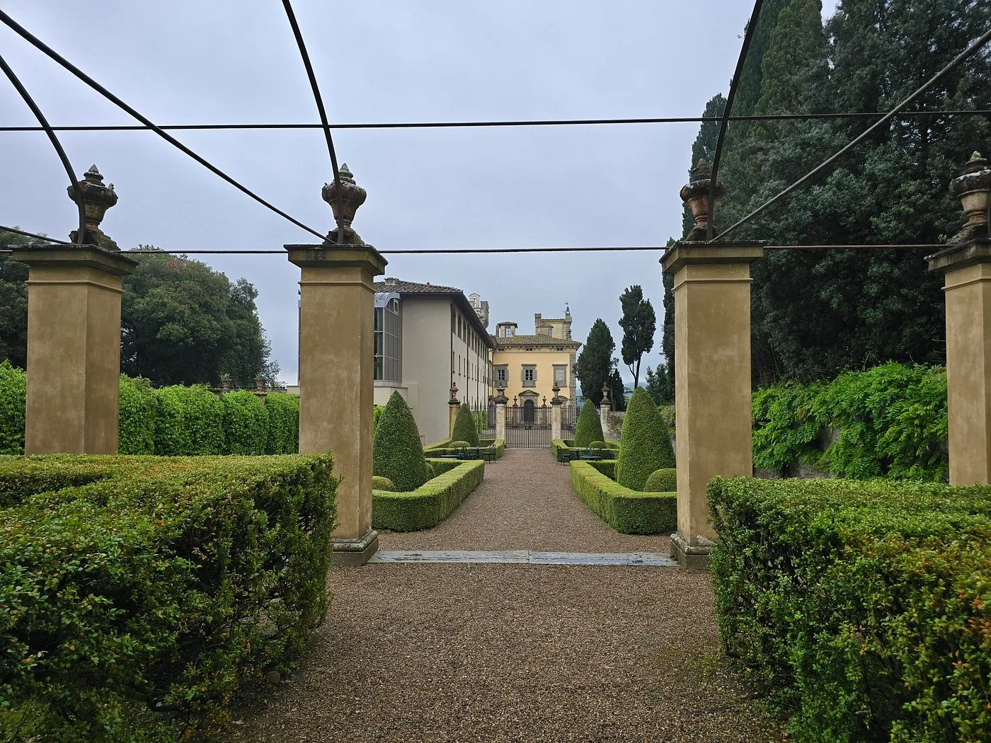 Viale del giardino con colonne in pietra e siepi che conduce alla villa in giornata nuvolosa
