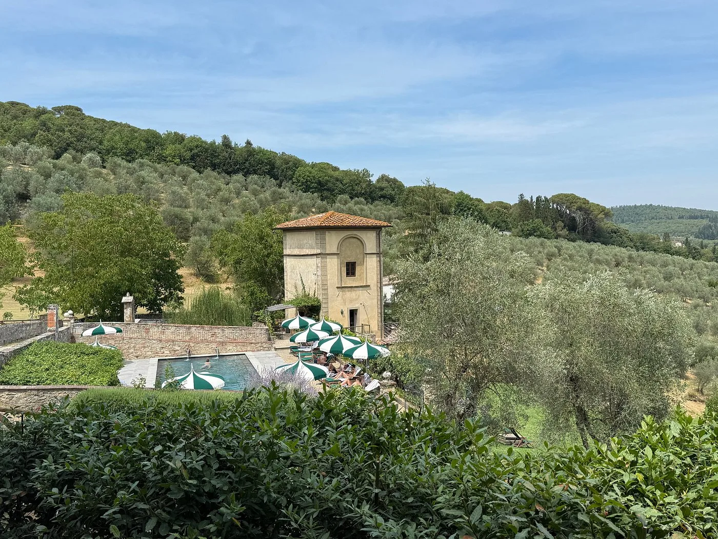Piscina con ombrelloni verdi e bianchi vicino a torre antica immersa negli uliveti