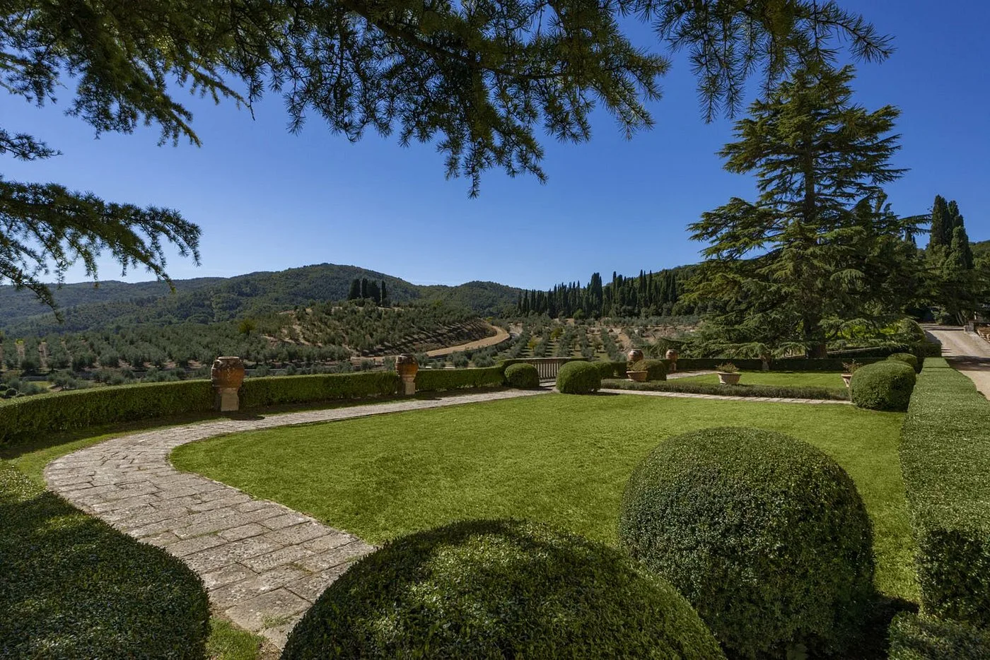 Giardino curato con siepi topiate e vista panoramica sulle colline con uliveti