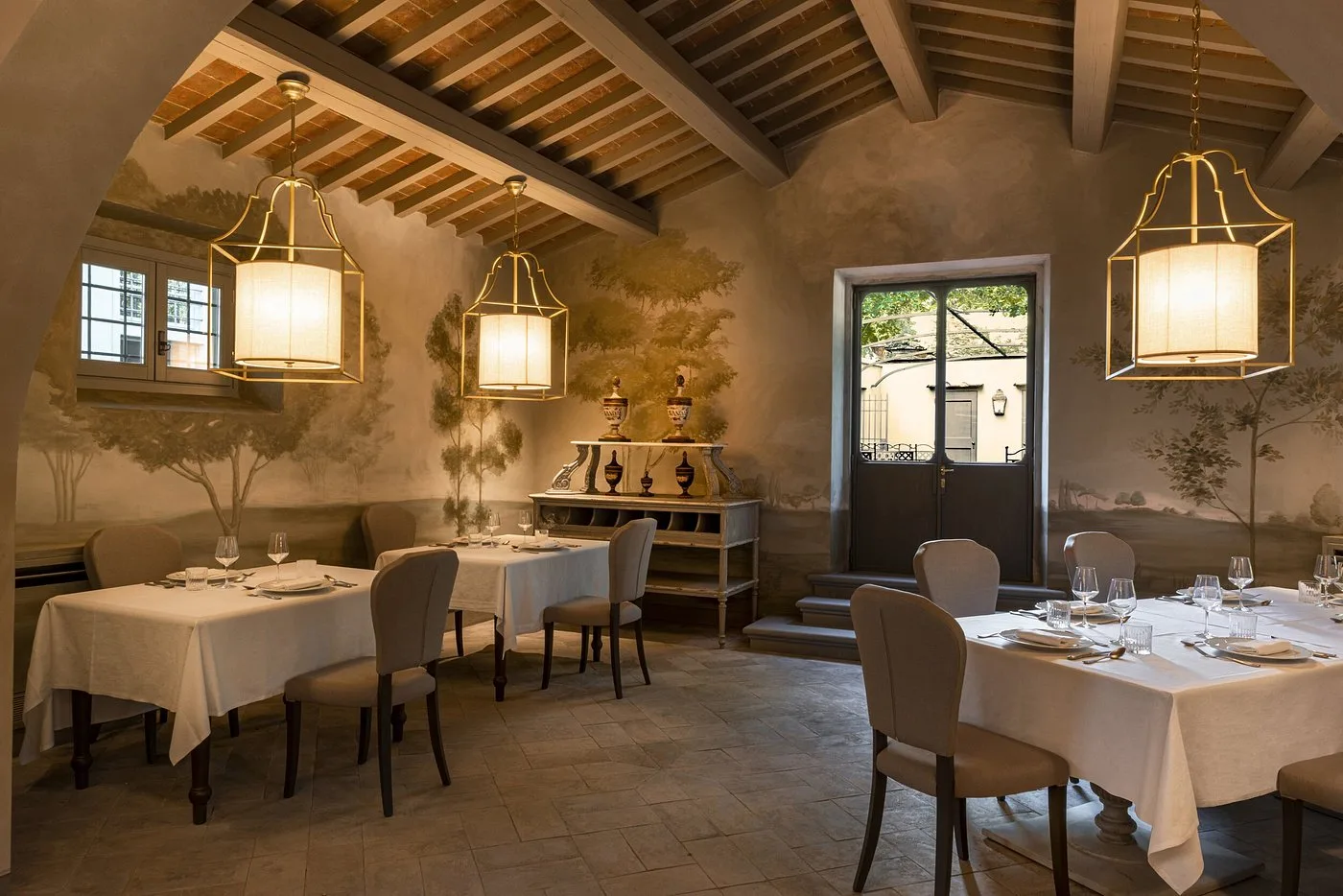 Ristorante interno con pareti affrescate, lampade a lanterna e tavoli eleganti