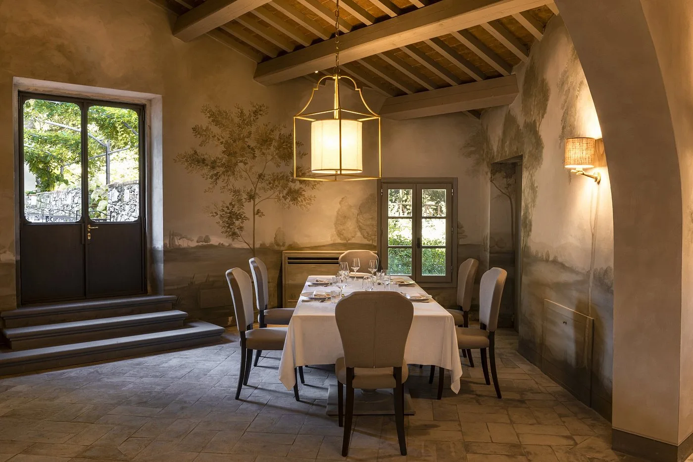 Sala da pranzo con affreschi paesaggistici, soffitto a travi in legno e tavolo apparecchiato