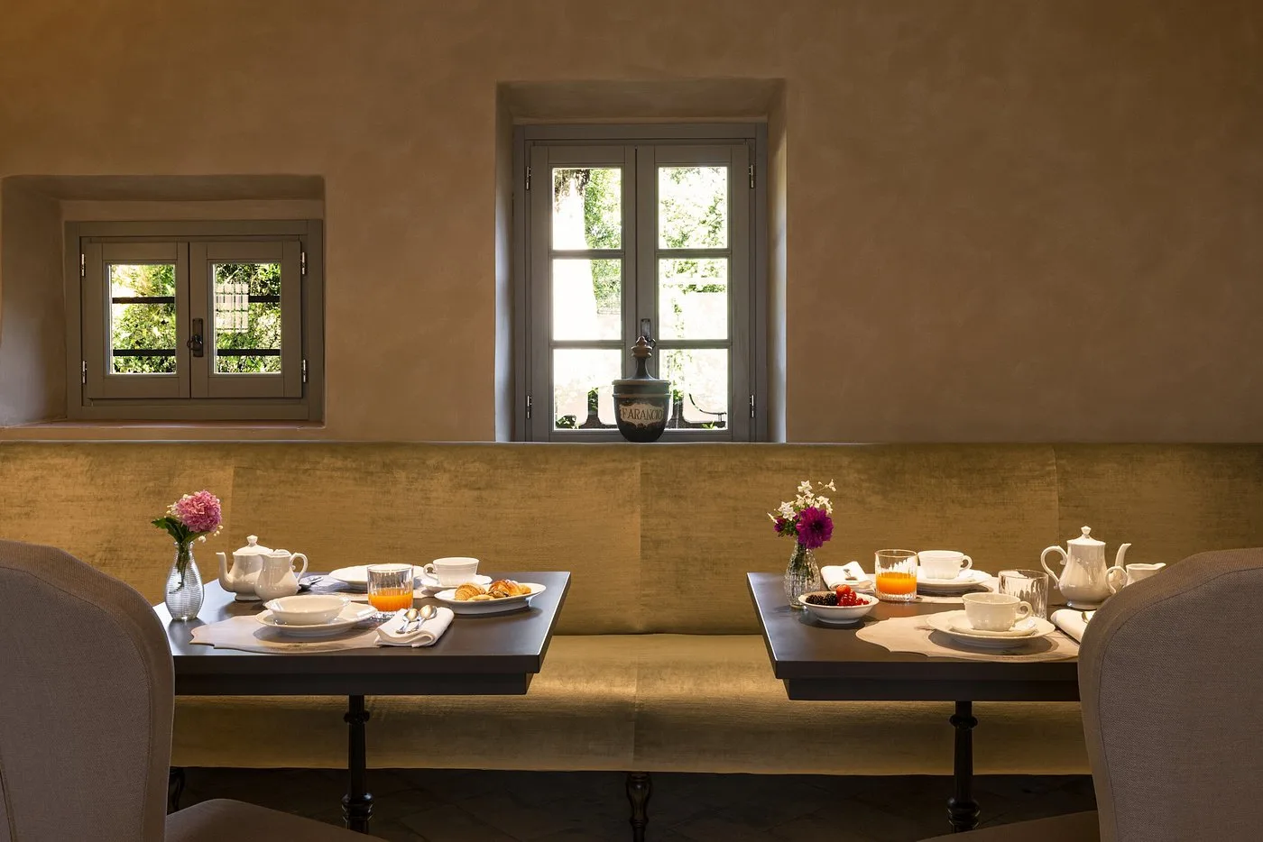 Sala colazione con tavoli apparecchiati, panca imbottita e finestre con vista giardino