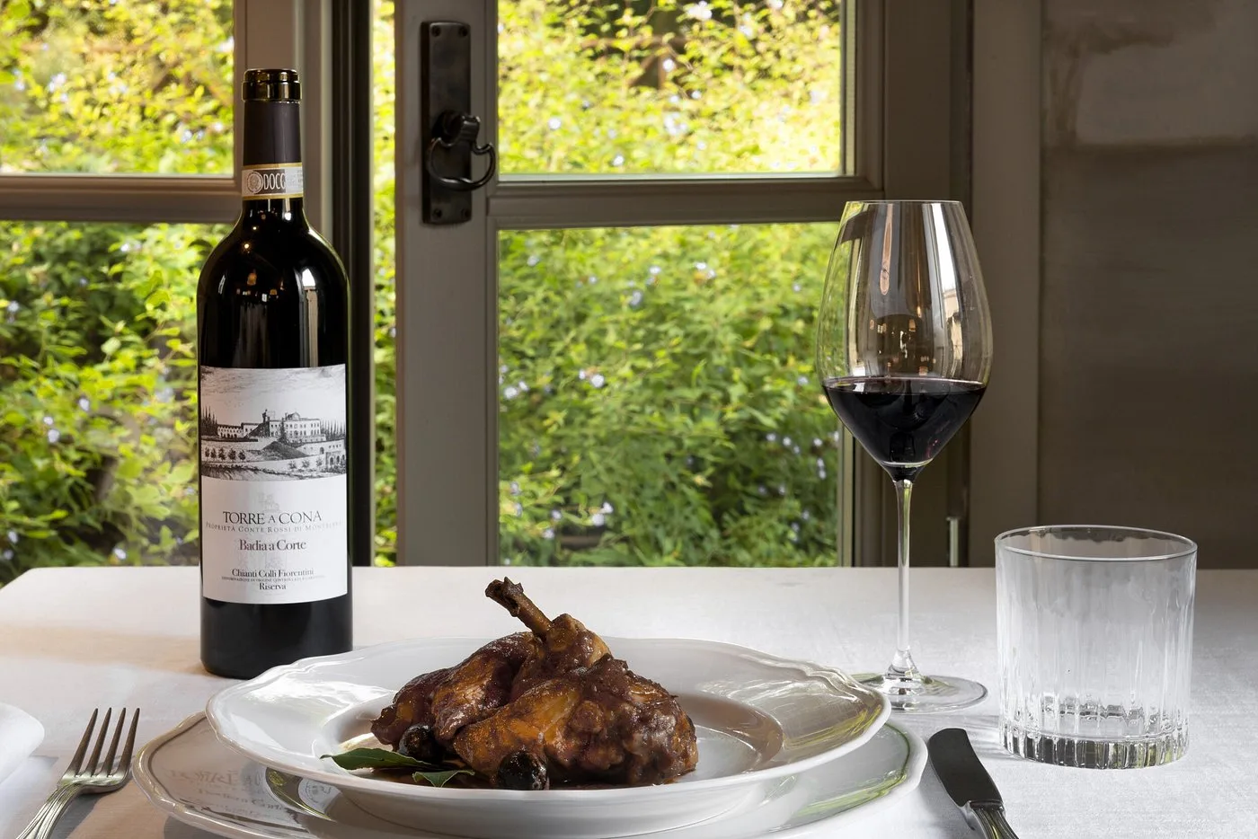 Piatto di carne con vino rosso Chianti Torre a Cona su tavolo con vista giardino