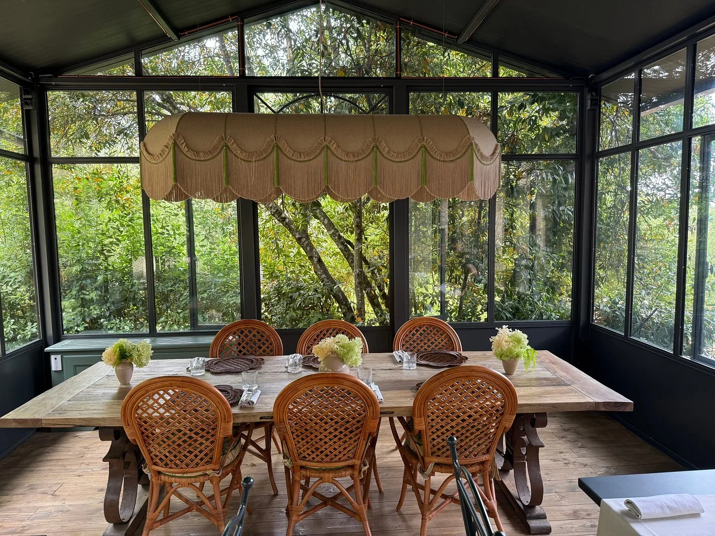 Veranda con vetrate, tavolo in legno e sedie in rattan affacciata sul giardino verde