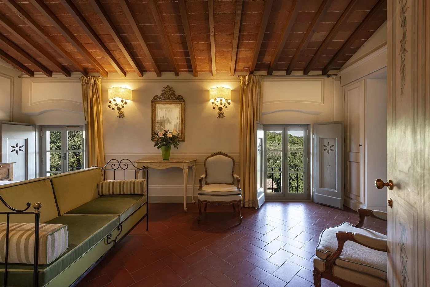 Suite con soffitto a travi in legno, divano verde, pavimento in cotto e finestre luminose