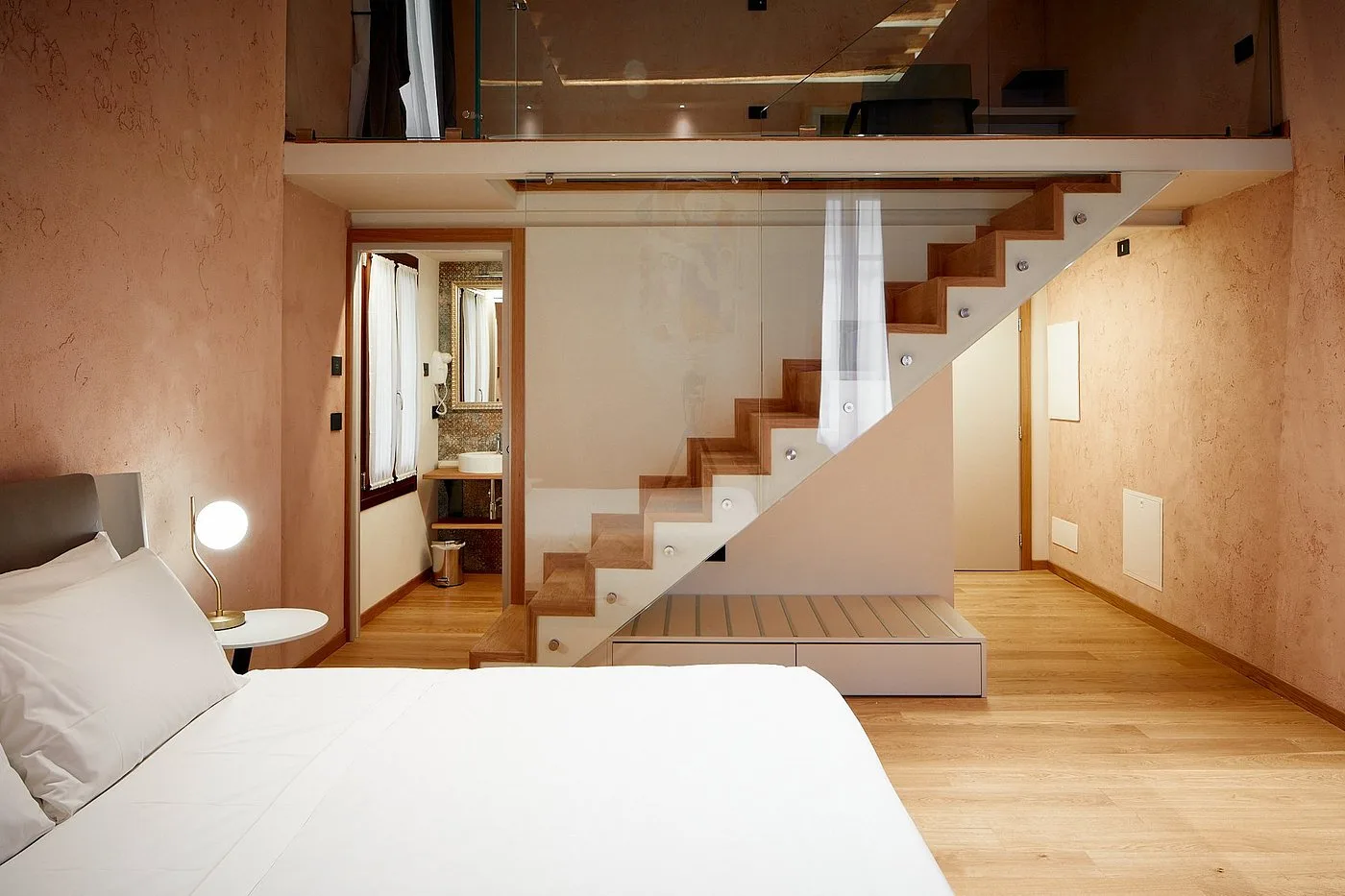 Camera matrimoniale con letto su due livelli, scala in legno e bagno visibile sullo sfondo