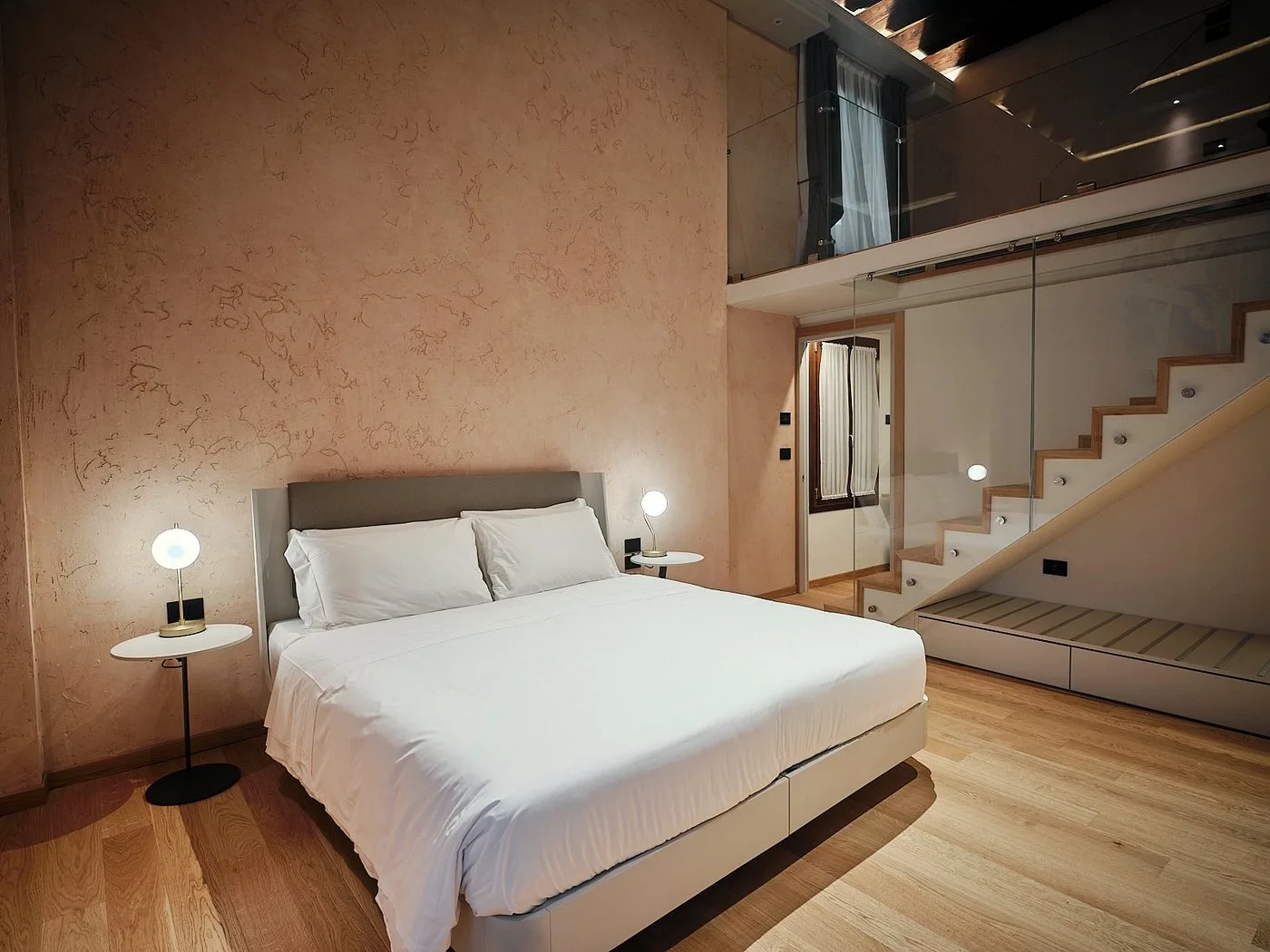 Camera doppia con letto king size, pareti rosa in stucco e scala verso soppalco