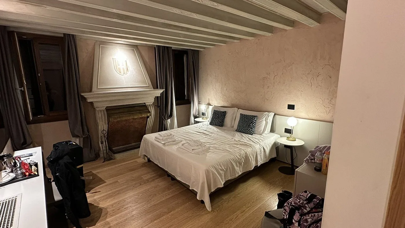 Camera con letto matrimoniale, camino in pietra con stemma e travi al soffitto