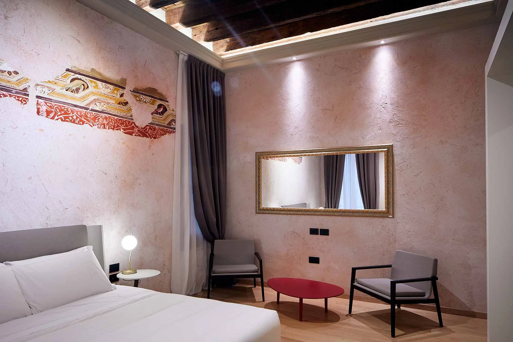 Camera con affresco decorativo, specchio dorato, poltrone e tavolino rosso