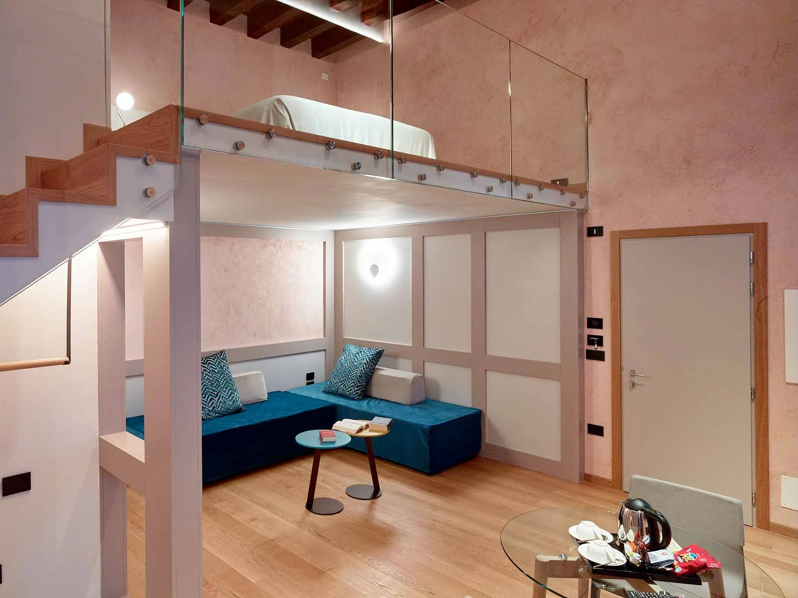 Suite loft con letto soppalcato, divano turchese e tavolino in vetro per la colazione