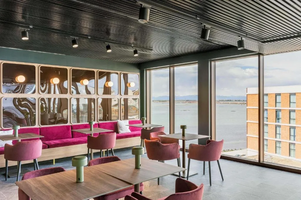 Sala interna con divani fucsia, tavoli e ampie vetrate sulla laguna