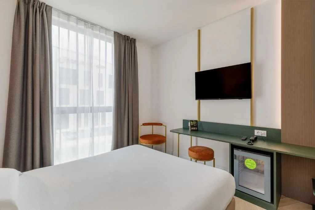 Camera moderna con letto, scrivania verde, TV e ampia finestra