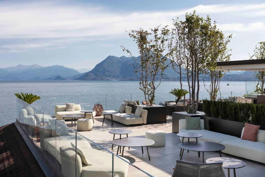 Terrazza lounge moderna con divani bianchi, alberi e vista sul lago e le montagne