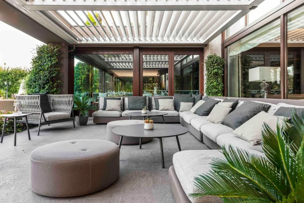 Salotto esterno con pergola, divani grigi e cuscini circondato dal verde