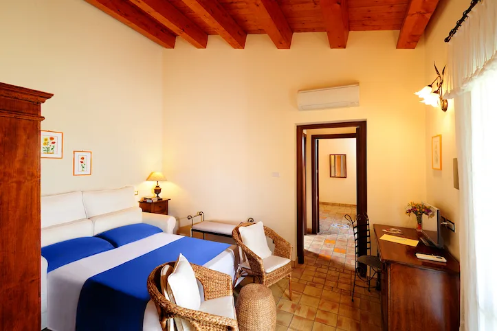 Camera con soffitto in travi di legno, letto blu e poltrone in vimini