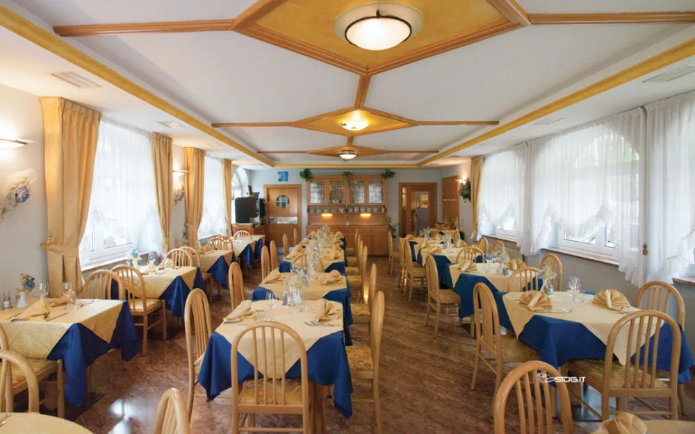 Sala da pranzo dell'hotel con tavoli apparecchiati in tovaglie blu e gialle e ampie finestre