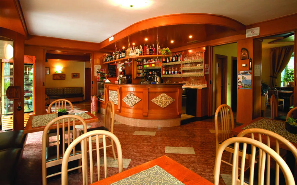 Bar dell'hotel con bancone in legno curvo, bottiglie e area lounge con tavolini