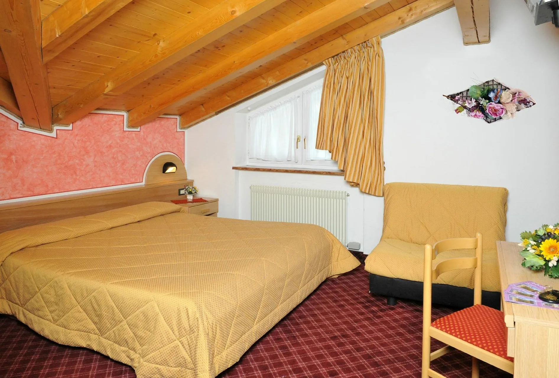 Camera mansardata con travi in legno, letto matrimoniale, poltrona e finestra con radiatore