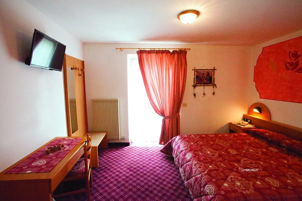 Camera matrimoniale con TV a parete, tende rosse e moquette a quadri viola