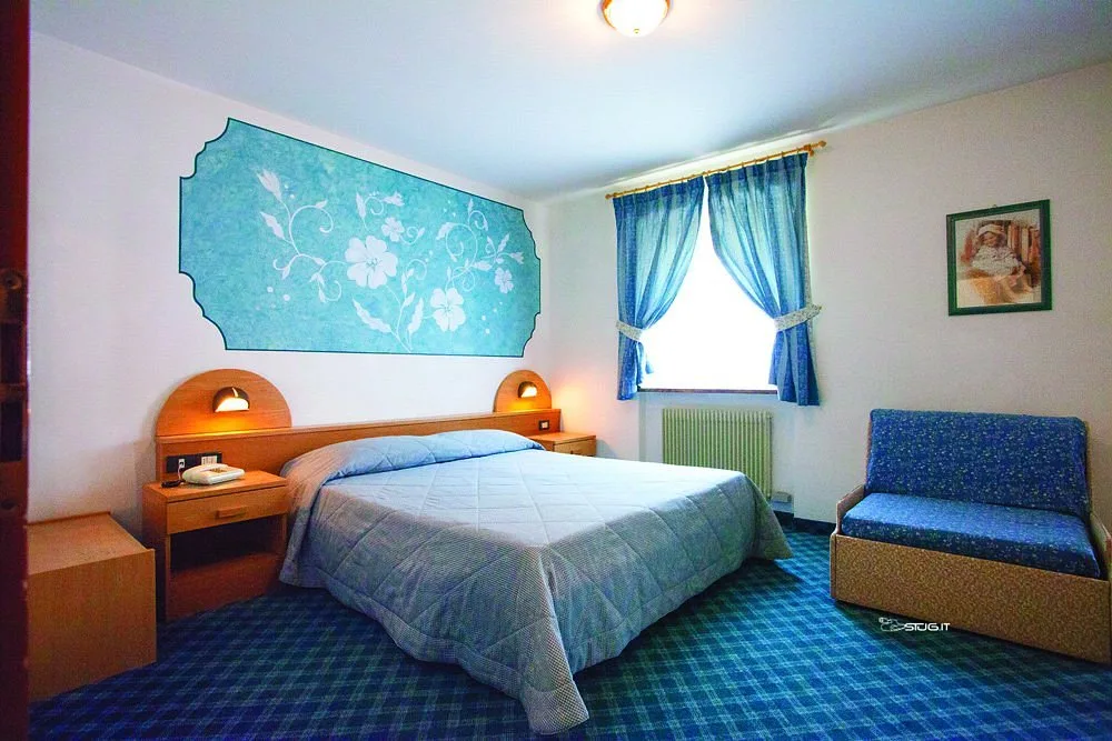 Camera con letto matrimoniale, poltrona blu, tende azzurre e decorazione floreale alla parete