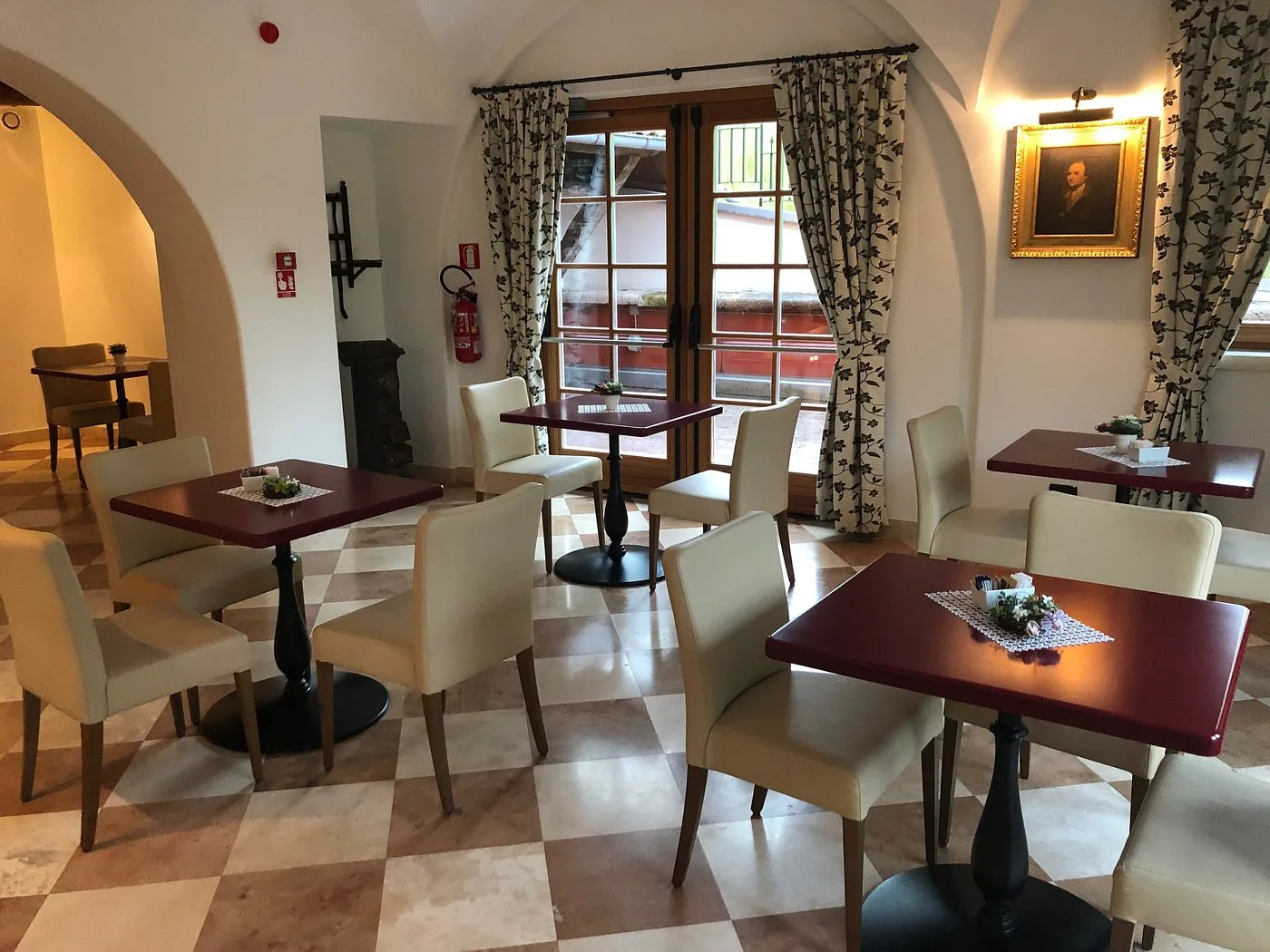 Sala da pranzo con tavoli rossi, sedie beige e pavimento a scacchi
