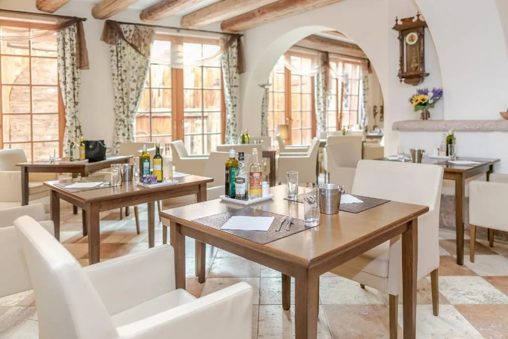 Sala ristorante luminosa con tavoli in legno, sedie bianche e ampie finestre