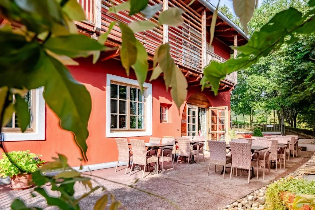 Terrazza esterna con parete rossa, tavoli e sedie in vimini immersa nel verde